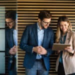 Board admins look at a tablet to discuss how to host an effective startup board meeting.