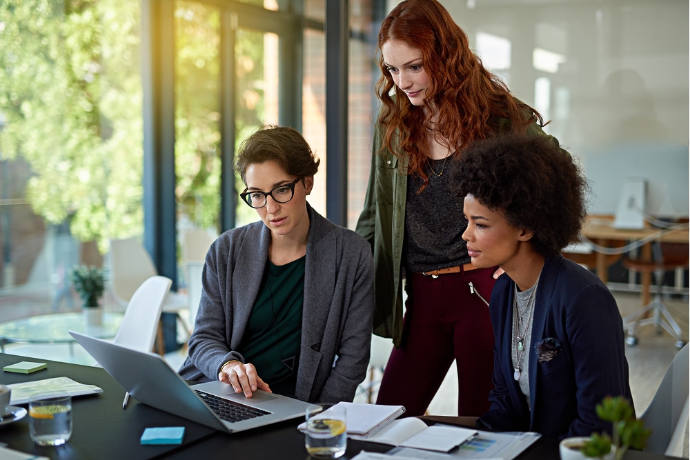Three women sit at laptop discussing AI governance framework.