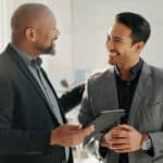 Two board members use a tablet to access an AI meeting minutes generator through their board portal.