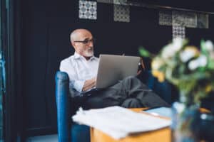 Man sits on couch using his laptop to compare best board management software for 2026.