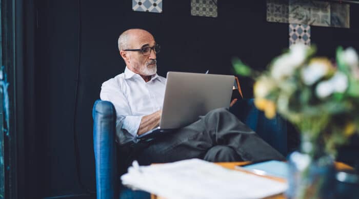 Man sits on couch using his laptop to compare best board management software for 2026.