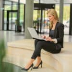 A board administrator sits in a common area, using her laptop to review board governance documents.