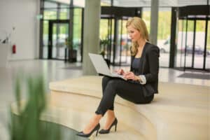 A board administrator sits in a common area, using her laptop to review board governance documents.
