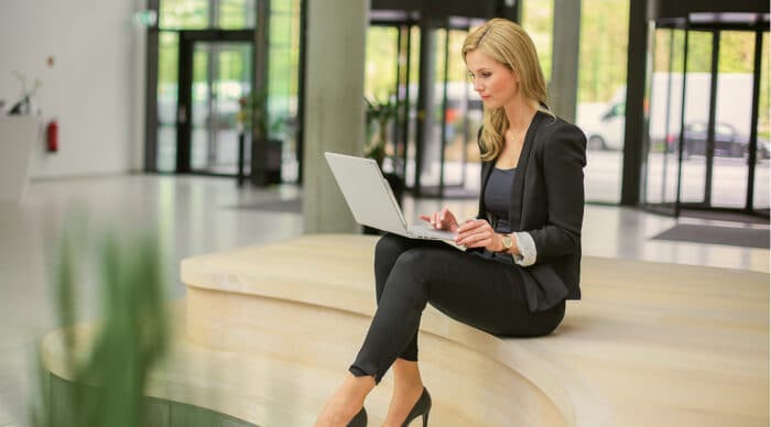 A board administrator sits in a common area, using her laptop to review board governance documents.