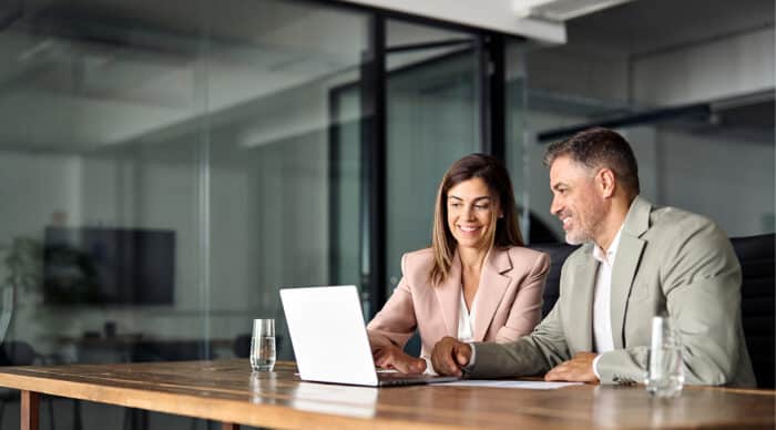 Two board members use a laptop equipped with hybrid board meeting tools to log in to a board meeting.