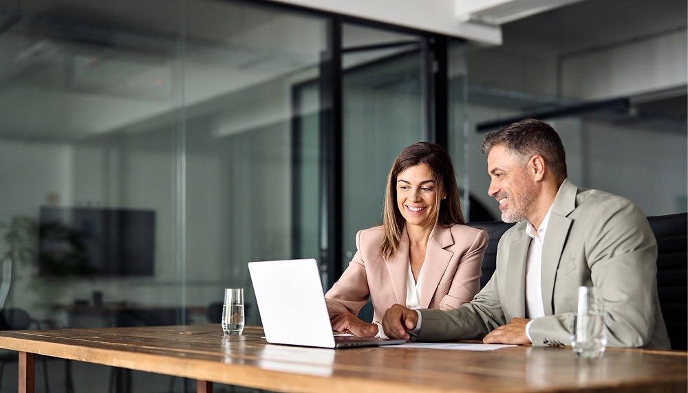 Two board members use a laptop equipped with hybrid board meeting tools to log in to a board meeting.